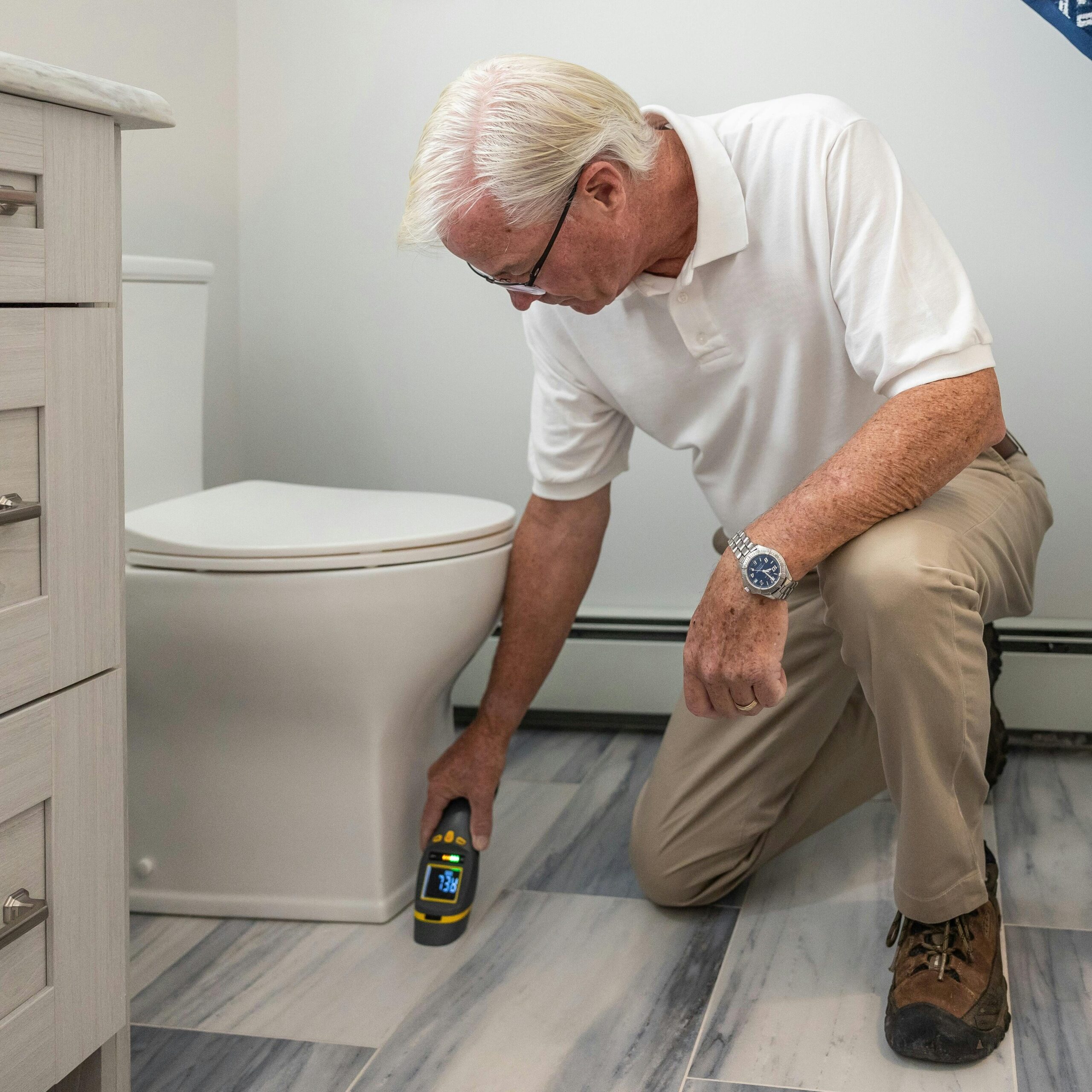 A senior man using a device to inspect a bathroom for maintenance or repair.